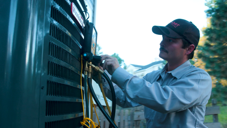 Professional HVAC technician using a digital multimeter to inspect a home heating and cooling unit.